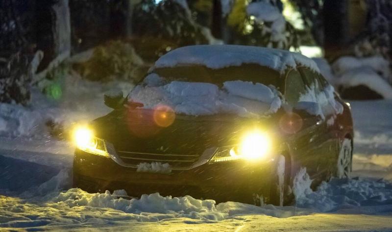A car with its lights on in the snow.