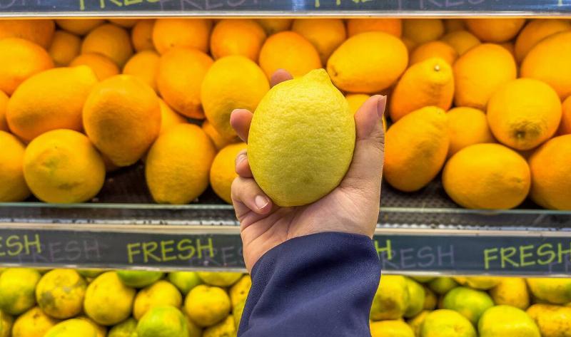 A person holding up a lemon in a grocery store.