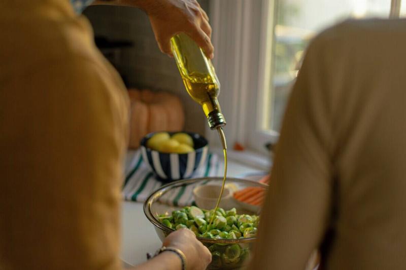 Person pouring olive oil onto a salad while another person watches
