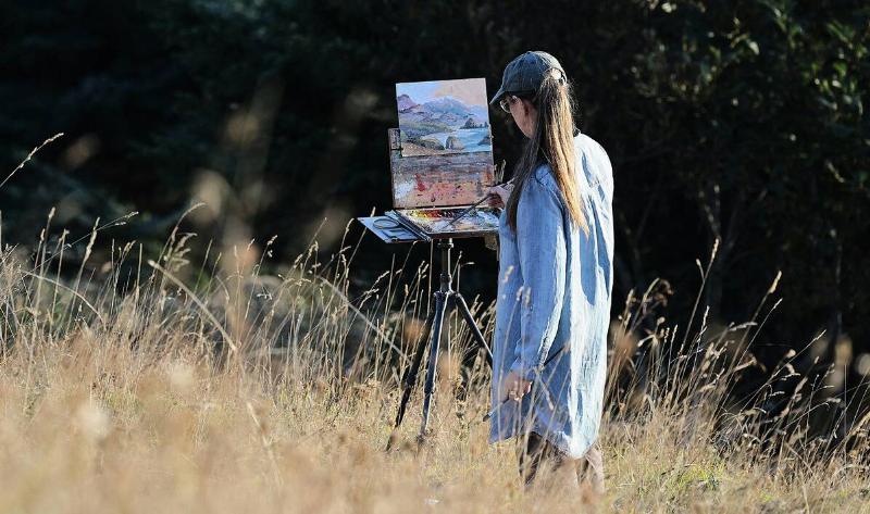 A woman standing in a field, painting the landscape before her.