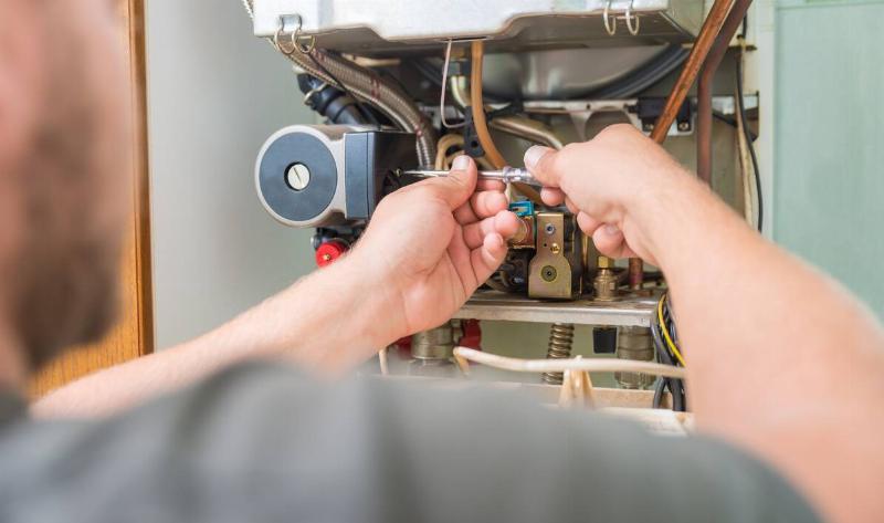 A repairman working on the internals in someone's furnace.