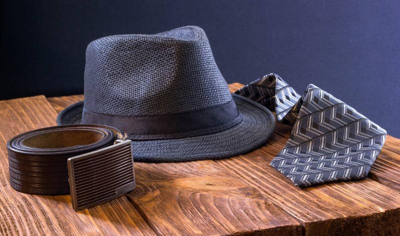 A belt, hat, and tie on a wooden table.