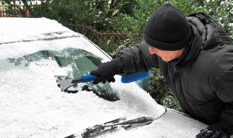 A man scraping ice off his windshield.