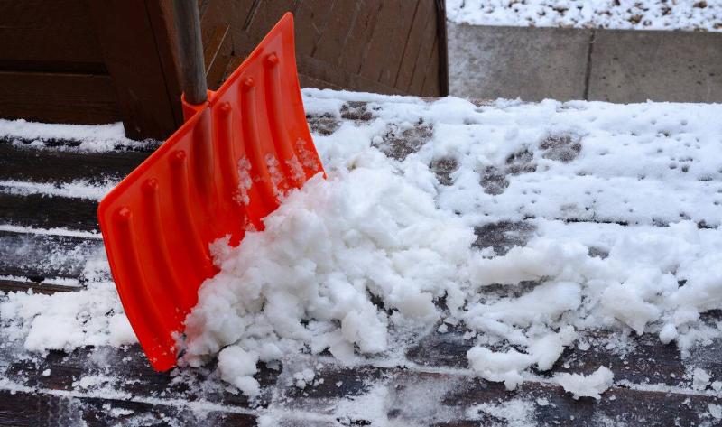 A snow shovel next to a pile of snow and ice on a porch.
