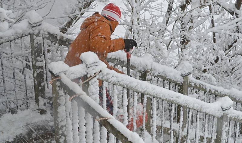 A person shoveling snow off their wooden steps.