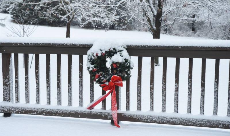 The railing of a deck covered in snow with a Christmas wreath on it.