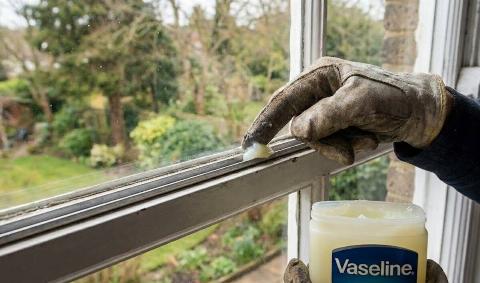 A person applying vaseline to the track of a window.