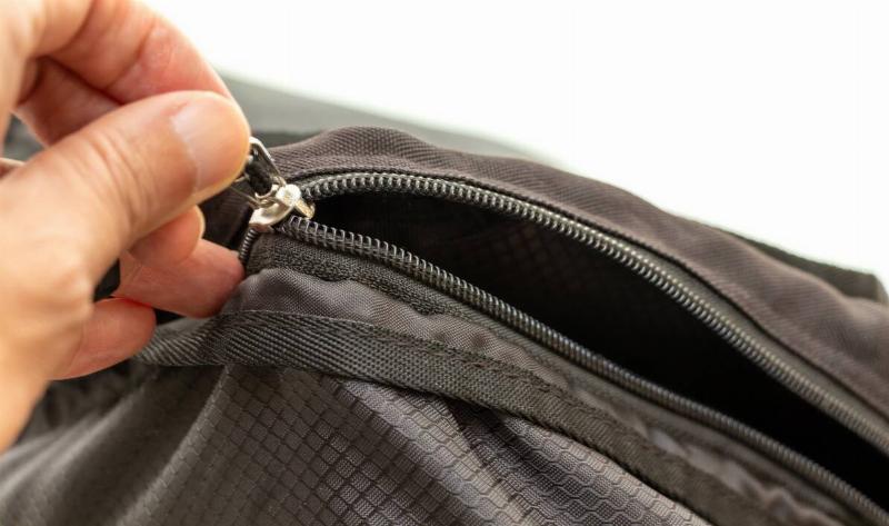 A person pulling a zipper on a bag closed.