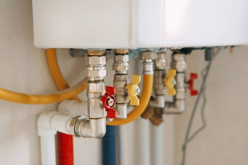 Close-up view of water heater pipes and valves in a utility room,  featuring colorful connectors and tubes. Essential components for 
heating system maintenance and operation. Gas boiler taps.