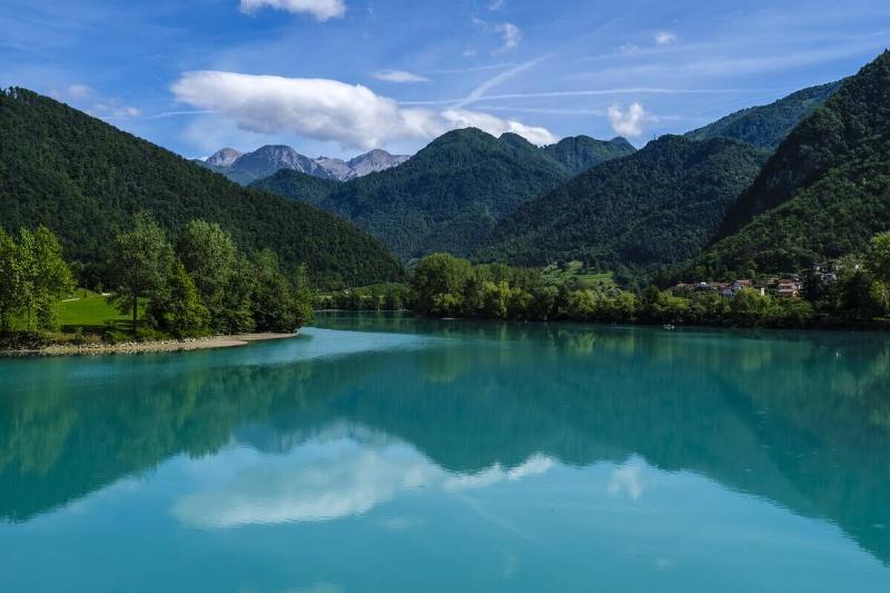 Turquoise waters of the Soca river reflecting forested mountains and a blue sky with white clouds in the distance.