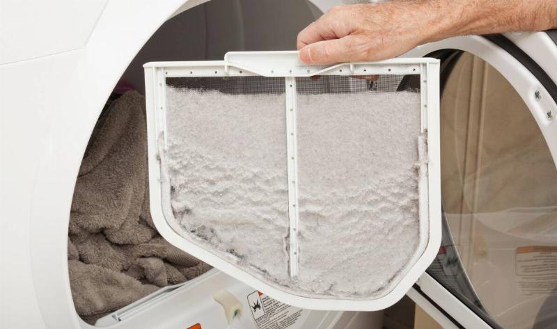 A person holding up the lint trap from their dryer that's full of lint.