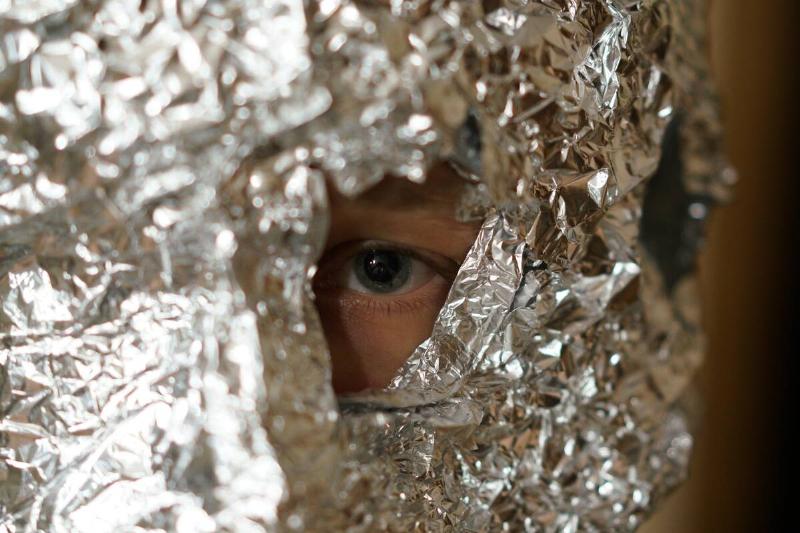 Boy looking through hole in aluminum foil. 