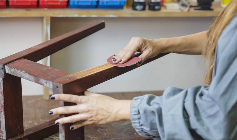 A woman sanding the leg of a chair.