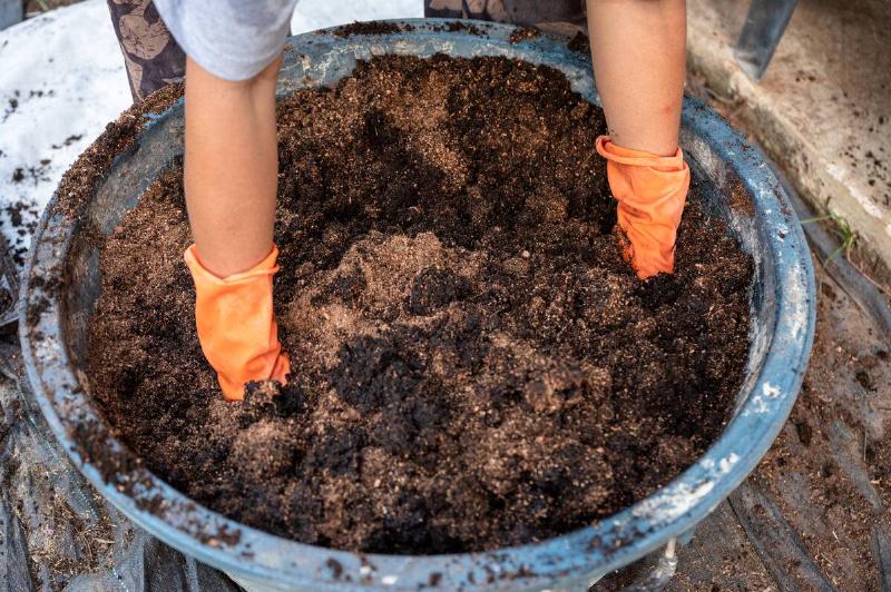 Farmer hand wearing gloves shoveling compost from manure, plant, and soil in bucket