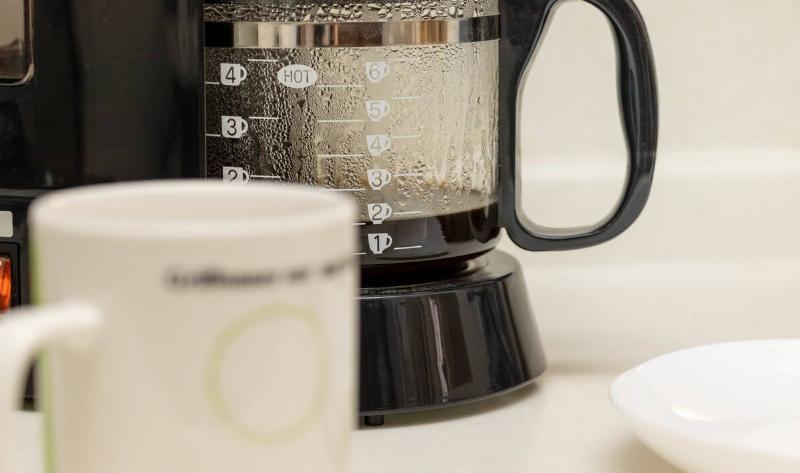 A close photo of a running coffee maker with a mug in the foreground.