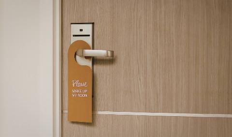 A hotel door with a hanger asking housekeeping to clean the room.
