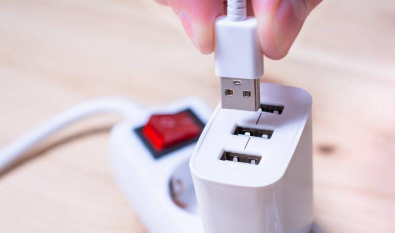 A person plugging a cable into a USB adapter that's plugged into a power bar.