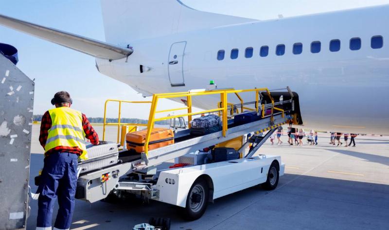 A luggage handler putting suitcases on a conveyor that's bringing them up to the plane.