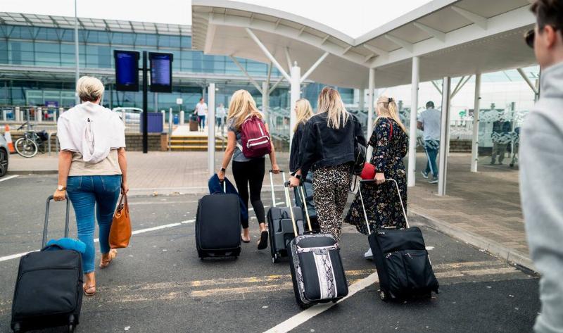 A family walking toward an airport, all with suitcases wheeling behind them.