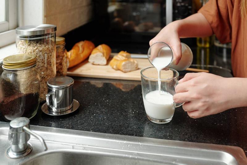 Close-up image of woman pouring milk in glass when making breakfast at kitchen counter