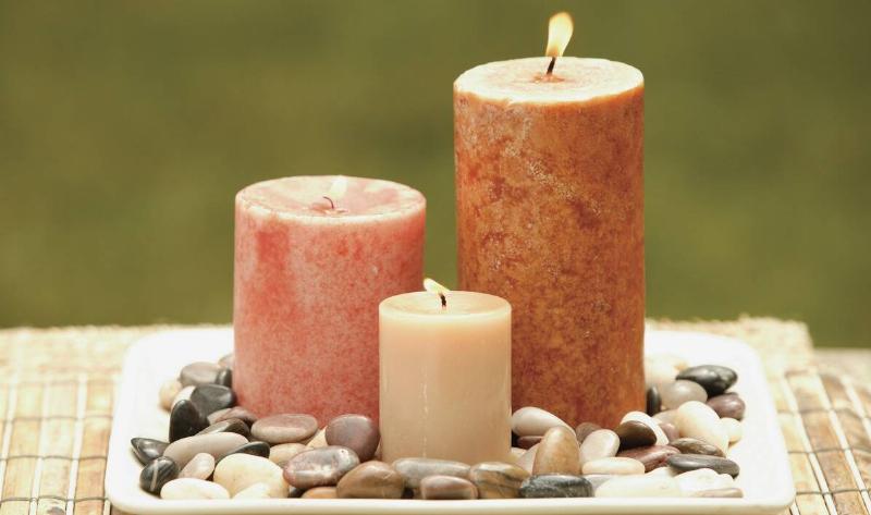 Three pillar candles of different colors atop a pebble tray.