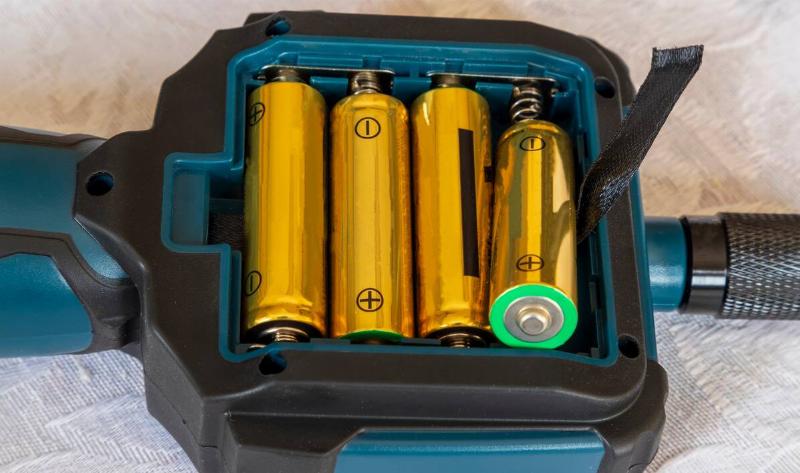 The battery port of a device, four batteries in it, one half popped out of its place.