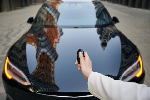 Women's hand pressing on remote control automobile alarm systems. Female arm holding car key on the background of luxure modern black auto.