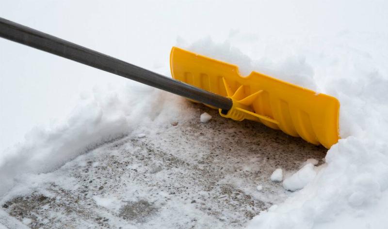 A yellow snow shovel pushing snow off a driveway.