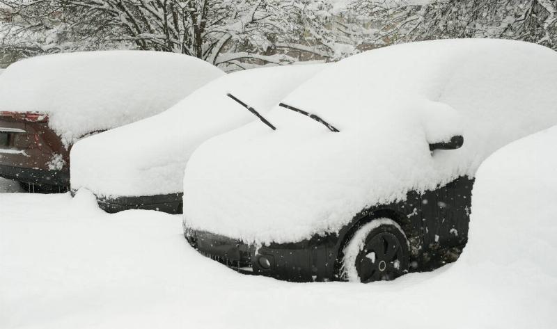 Cars in a parking lot piled high with snow after a storm.