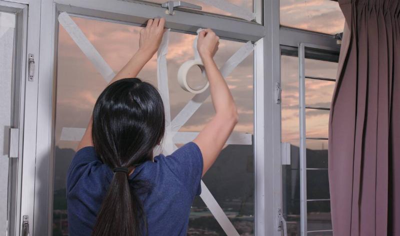 A woman putting storm tape on her window.