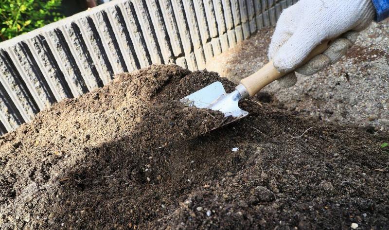 A person digging in a pile of dirt with a trowel.