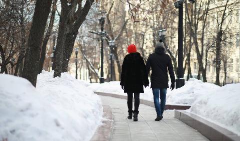 A couple walking through a snowy city part, holding hands.