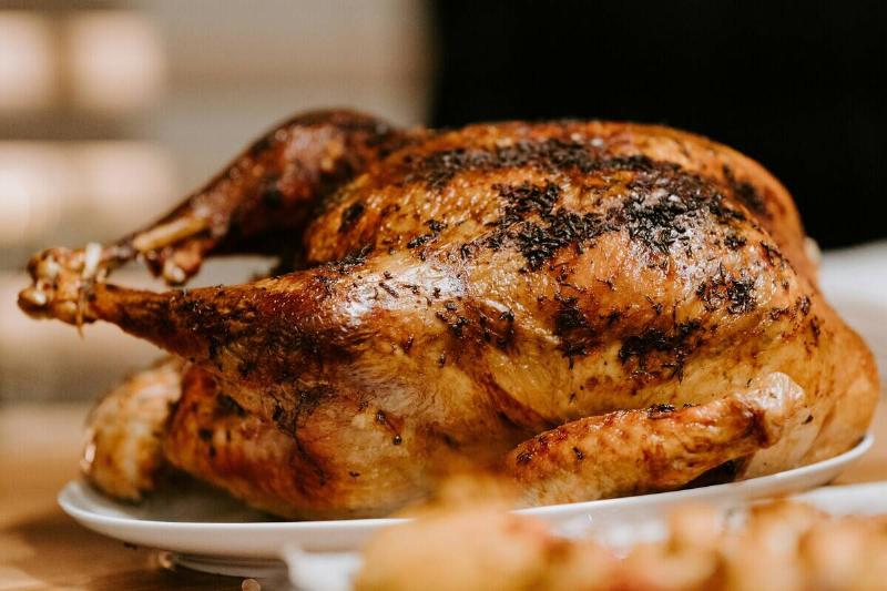 Whole roast chicken on a plate, surrounded by other food on a wooden table