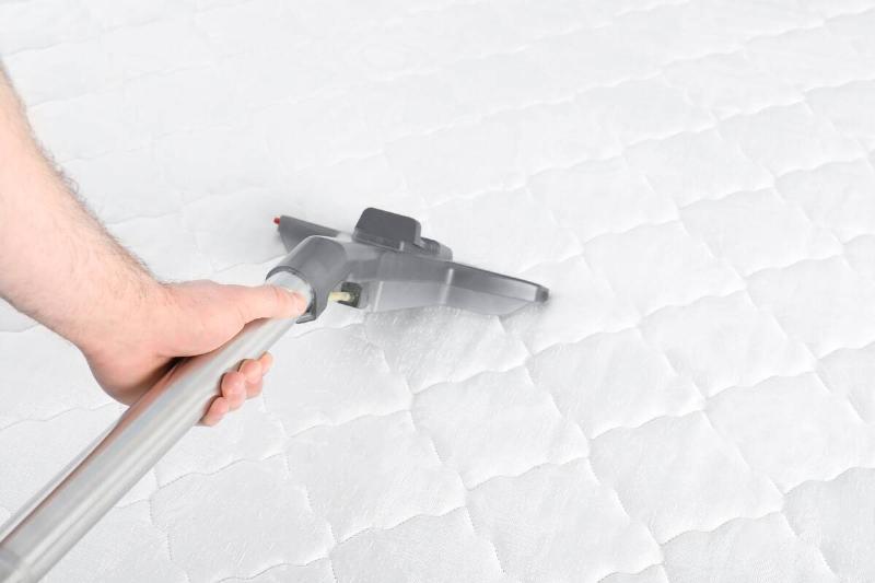 A hand vacuuming a mattress. 