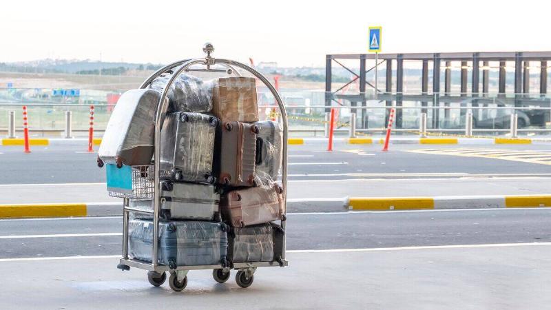 A porter cart full of suitcases by the road outside the airport
