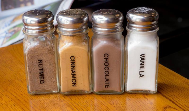 Four old salt shakers being used to house powdered seasonings, including one for cinnamon.