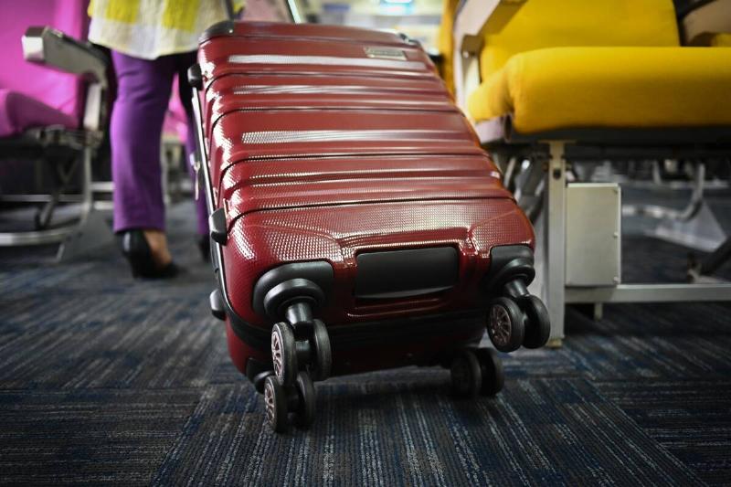 Unrecognizable female tourist with suitcase walking the aisle on plane. Travel and summer vacation concept.