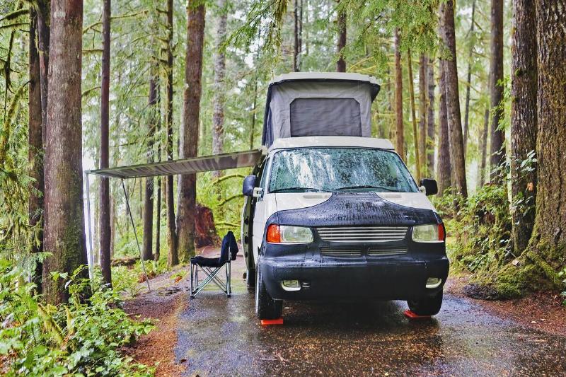 Camper van with awning parked at campsite in a forest.