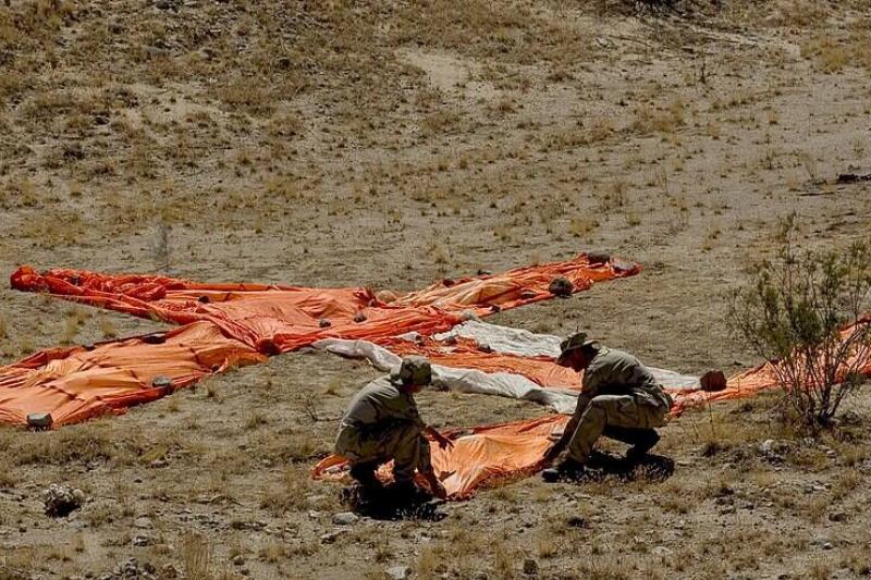 Photographer's Mate 2nd Class James Orosco and Aviation Structural Mechanic 3rd Marty Bullwinkel use parachute material to improvise a ground-to-air-signal to catch the attention of over-flying aircraft during desert survival training.