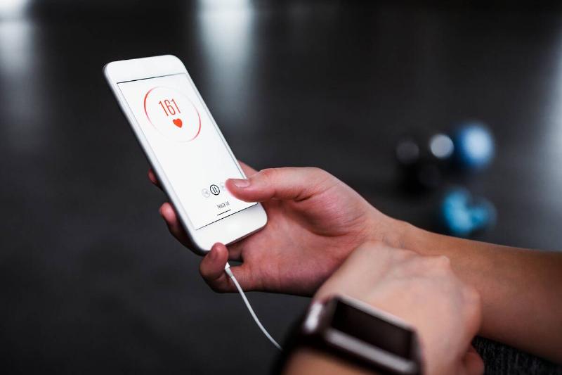 A hand holding a phone showing a heart rate tracker and a fitness tracker. 