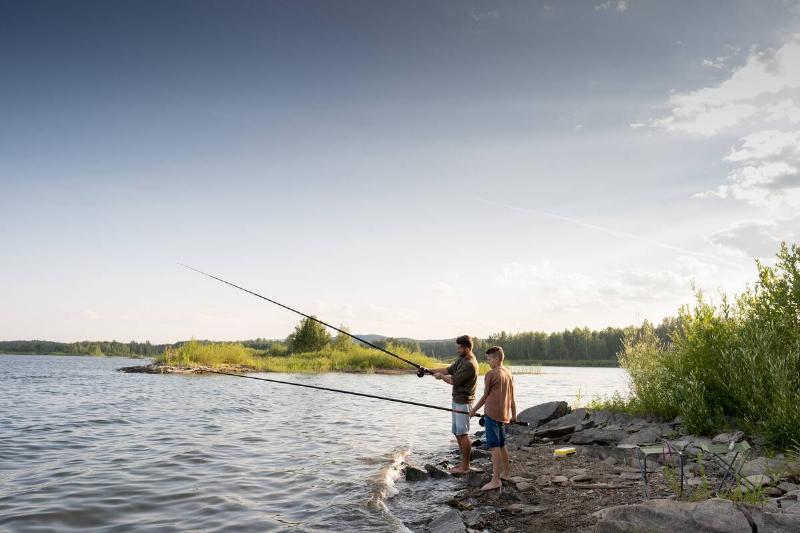 Active man and teenage boy with rods fishing by lake on summer weekend.