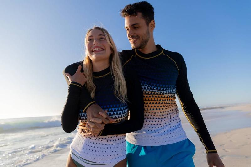 Man and woman wearing sunshirts on the beach. 