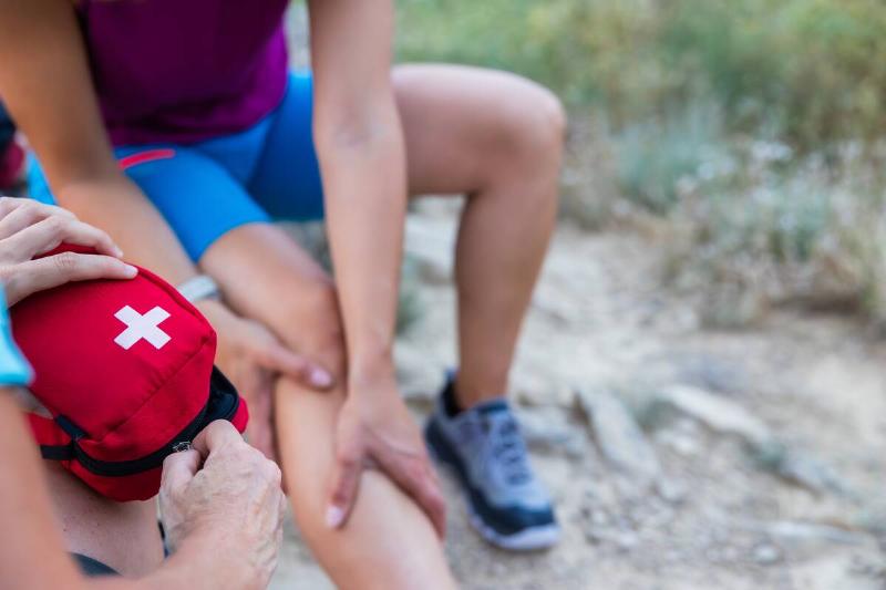 A close view of a woman holding her injured leg while a companion opens a red first aid kit.