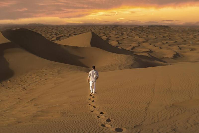 A man walking through sand dunes in the desert. 