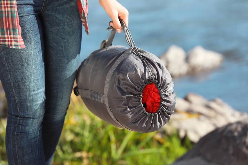 Female camper with sleeping bag outdoors.