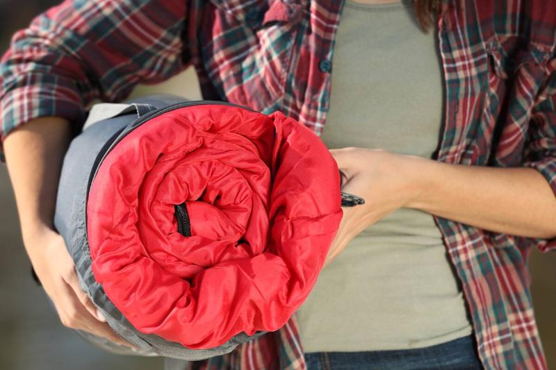 Female camper with sleeping bag outdoors.