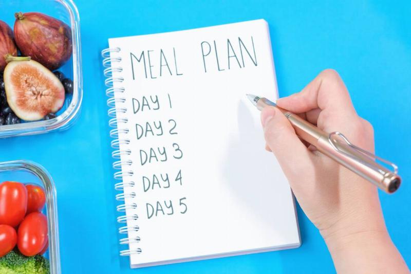 A hand is writing a meal plan in a notebook. 