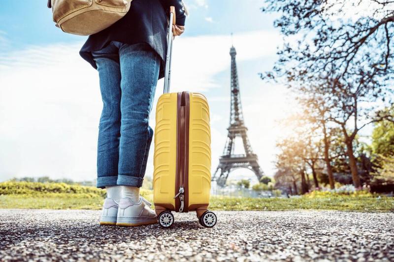 Happy tourist with luggage visiting Eiffel Tower in Paris, France.