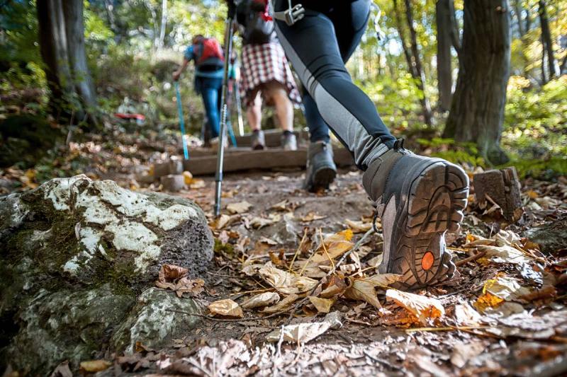 Hiker woman with trekking sticks climbs steep on mountain trail, focus on boot.
