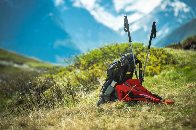 Hikers Backpack, Coat and Trekking Poles on a Sunny Mountain Trail.